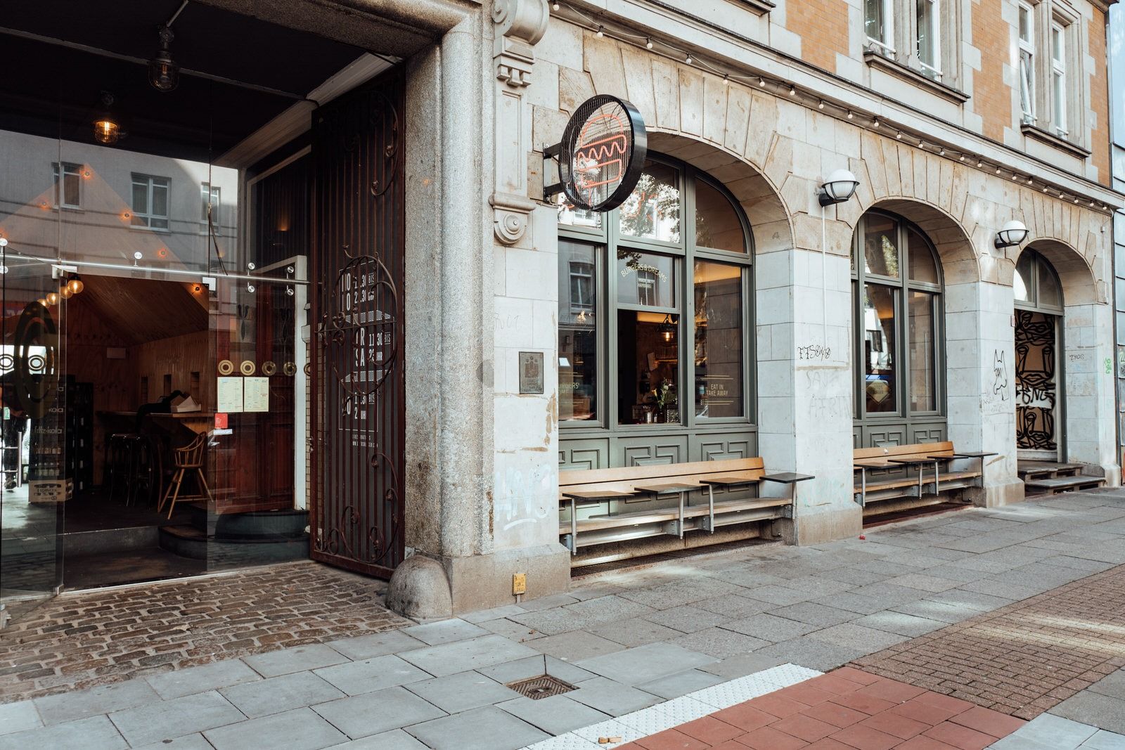 Außenansicht von "Otto's Burger" mit Glasfront, offenem Eingang, Rundbogenfenstern und seitlichem Blick in den Gastraum.