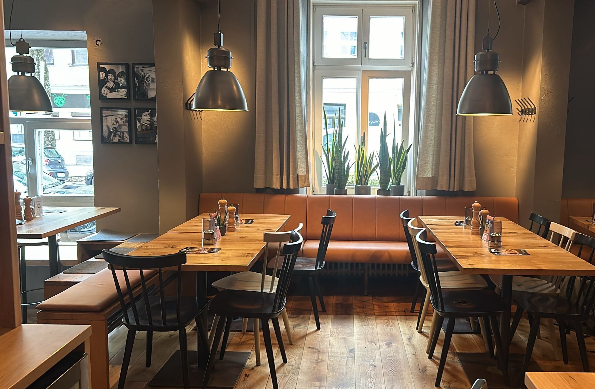 Innenansicht von "Ruff's Burger" mit Holztischen, schwarzen Stühlen, brauner Polsterbank, großen Fenstern und Pflanzen auf der Fensterbank.