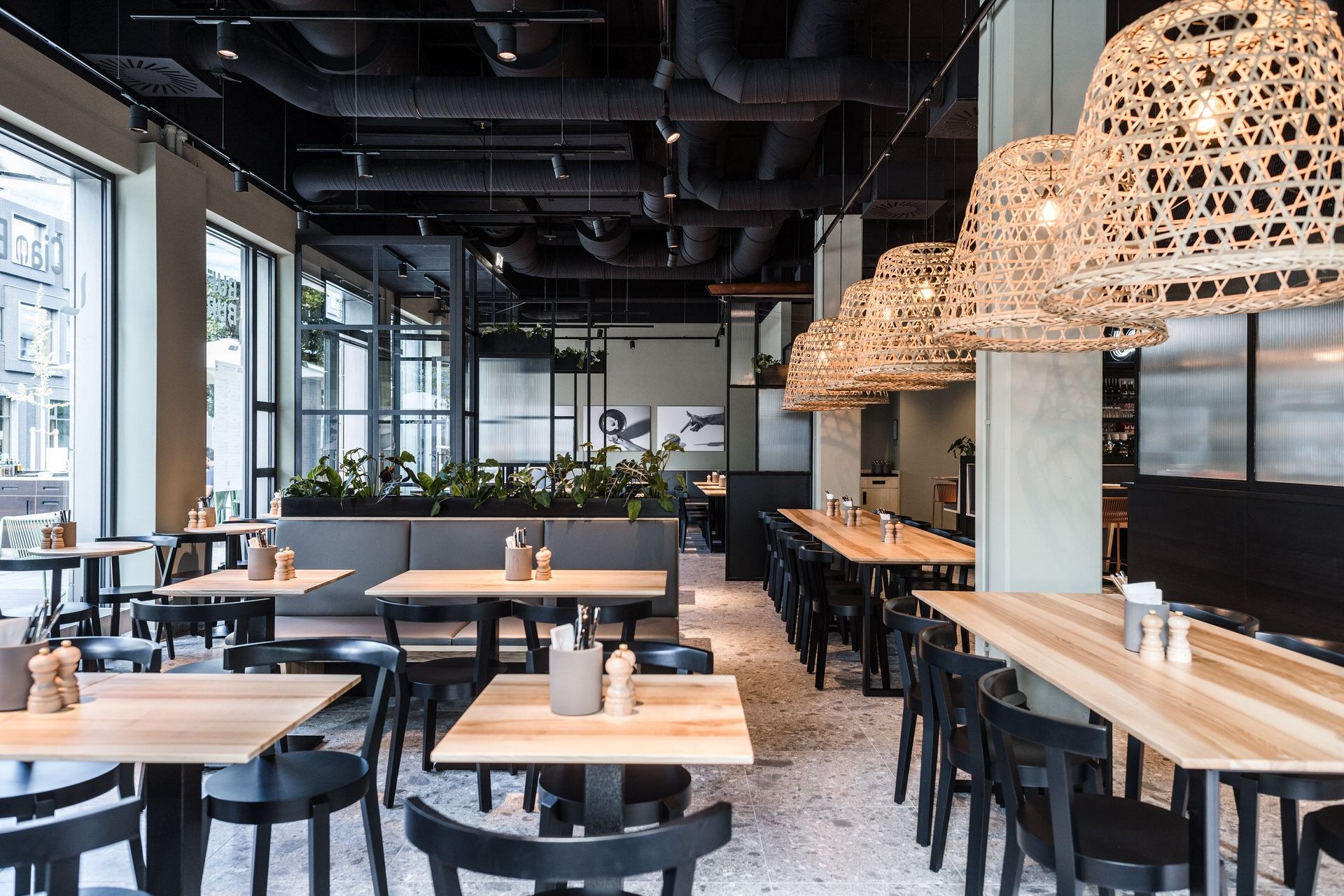 Innenansicht von "Ruff's Burger" mit Holztischen, Rattanhängelampen, schwarzen Stühlen, Polsterbänken und Pflanzen.