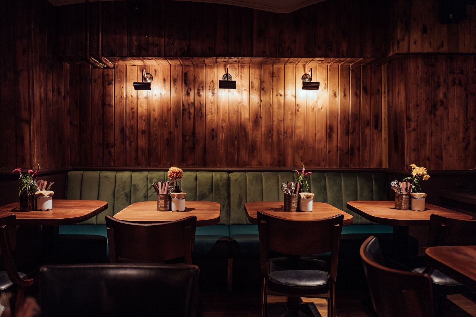 Innenansicht von "Otto's Burger" mit grüner Polsterbank, Holztischen, Holzstühlen und vertäfelter Holzrückwand mit Lampen.