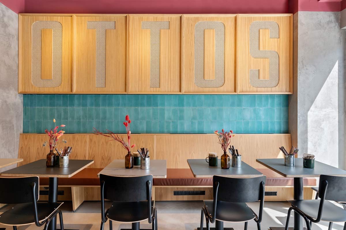 Innenansicht von "Otto's Burger" mit Sitzbereich, Holztischen, schwarzen Stühlen, grünen Wandfliesen und großem OTTO'S Schriftzug.