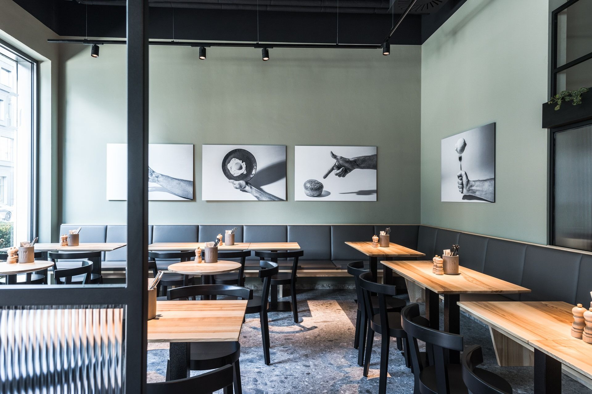 Innenansicht von "Ruff's Burger" mit Holztischen, schwarzen Stühlen, grauer Polsterbank, grüner Wand mit Schwarz-Weiß-Fotografien.