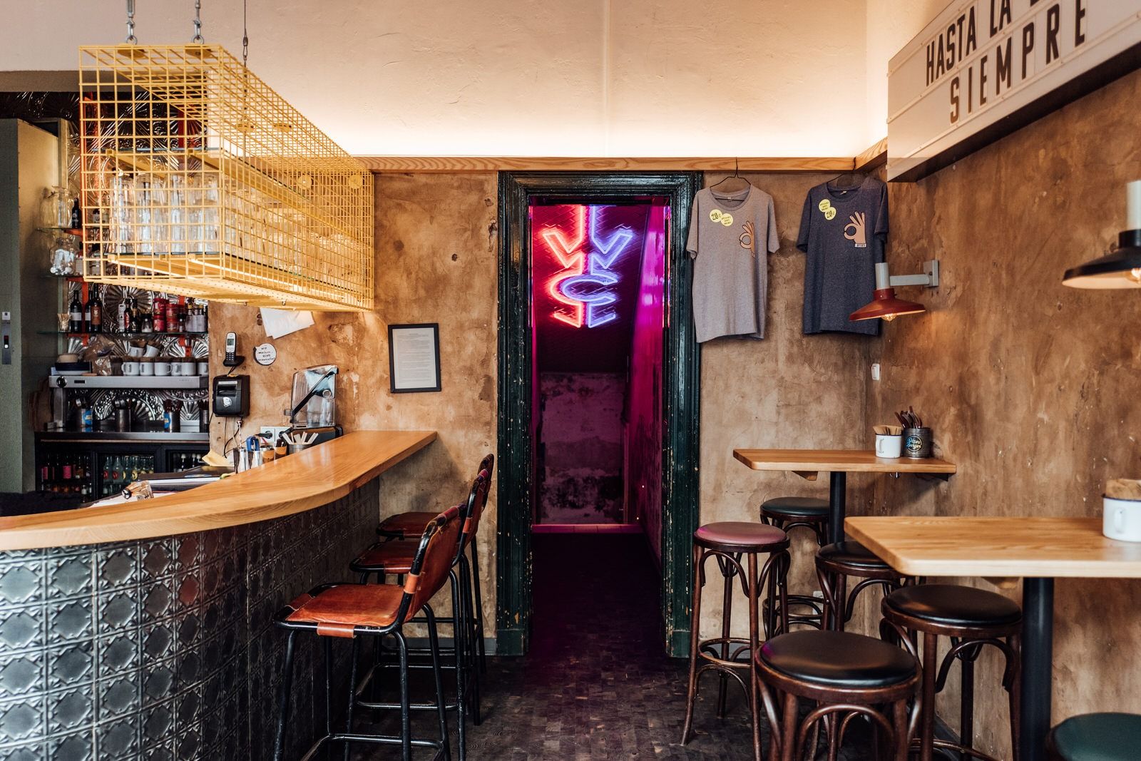 Barbereich von "Otto's Burger" mit Holztheke, Metallverkleidung, Neon-WC-Schriftzug im Hintergrund und gelbem Gläserregal.