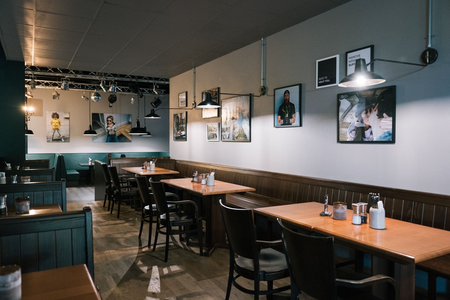 Innenansicht von "Ruff's Burger" mit Holztischen, dunklen Holzstühlen, Polsterbänken, Wandbildern und Industriebeleuchtung.