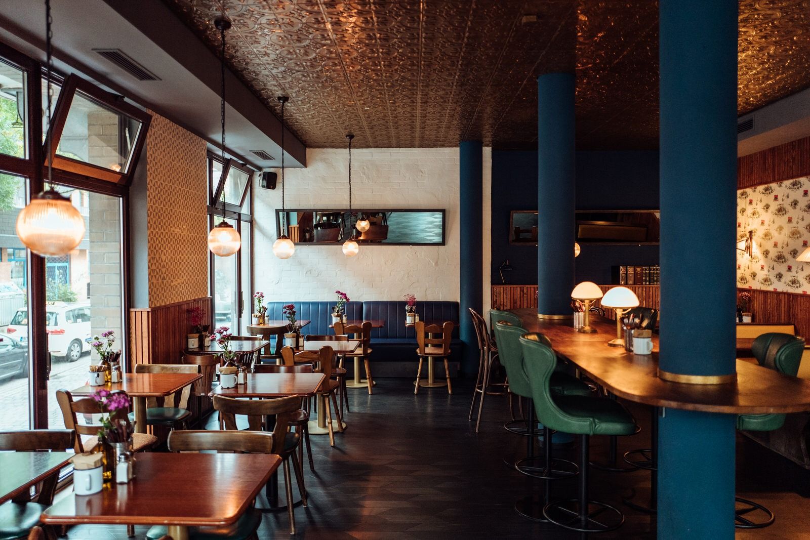 Innenansicht von "Otto's Burger" mit Holztischen, grünen Barhockern, Lampen, blauen Säulen und großen Fensterfronten.