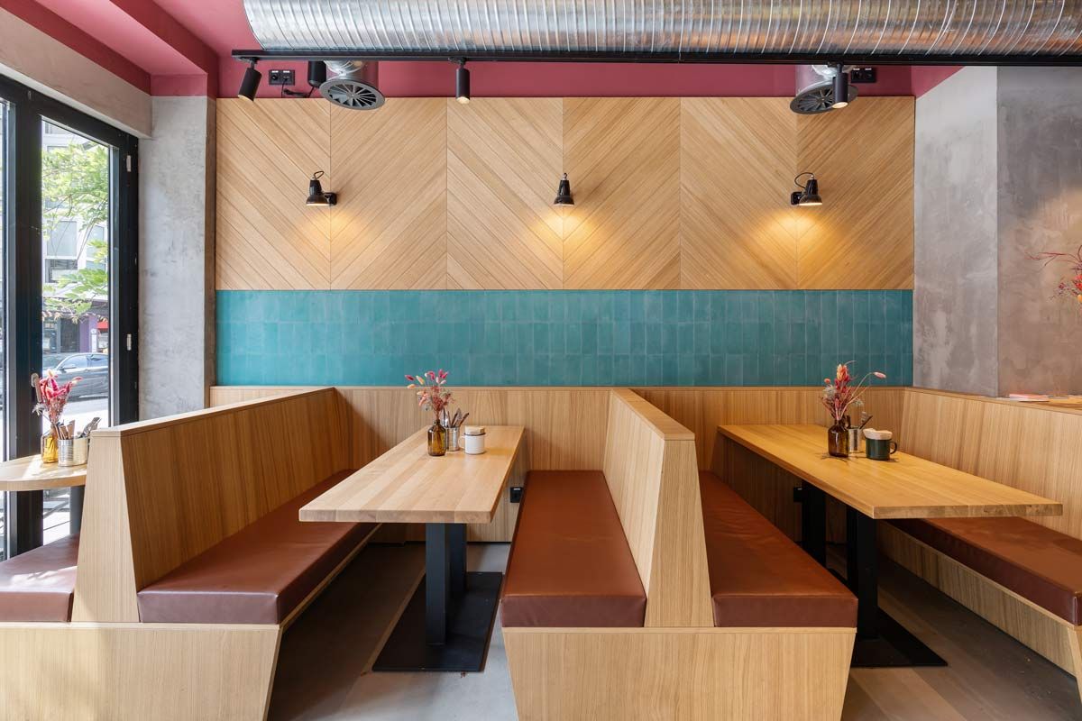 Innenansicht von "Otto's Burger" mit Holztischen, braunen Sitzbänken, grünen Wandfliesen und diagonalen Holzpaneelen.
