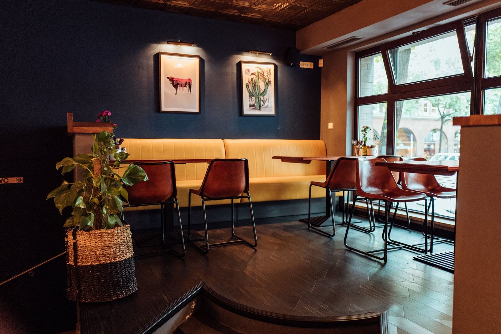 Innenansicht von "Otto's Burger" mit gelber Polsterbank, dunklen Holztischen, Lederstühlen, Pflanzen und Wandbildern.