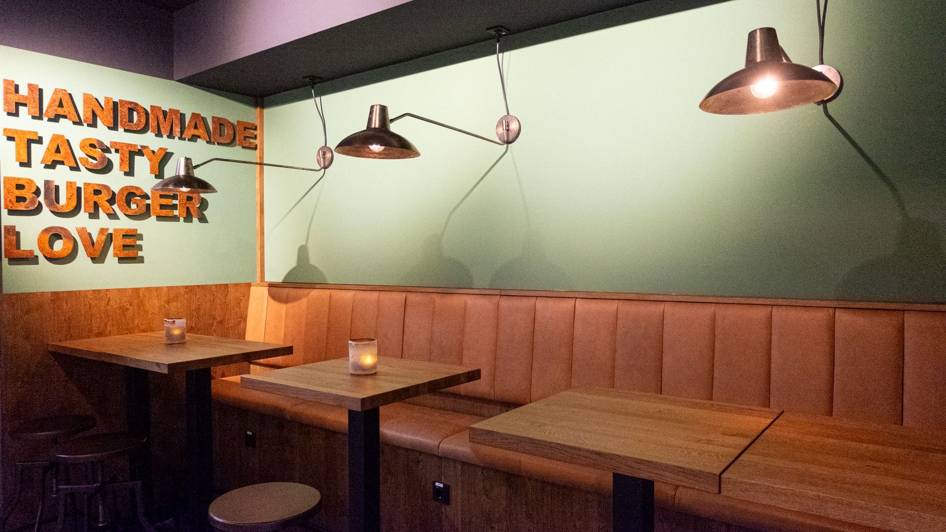 Innenbereich von "Ruff's Burger" mit grüner Wand, gepolsterten Sitzbänken, Holztischen und Wanddeko "Handmade Tasty Burger Love".