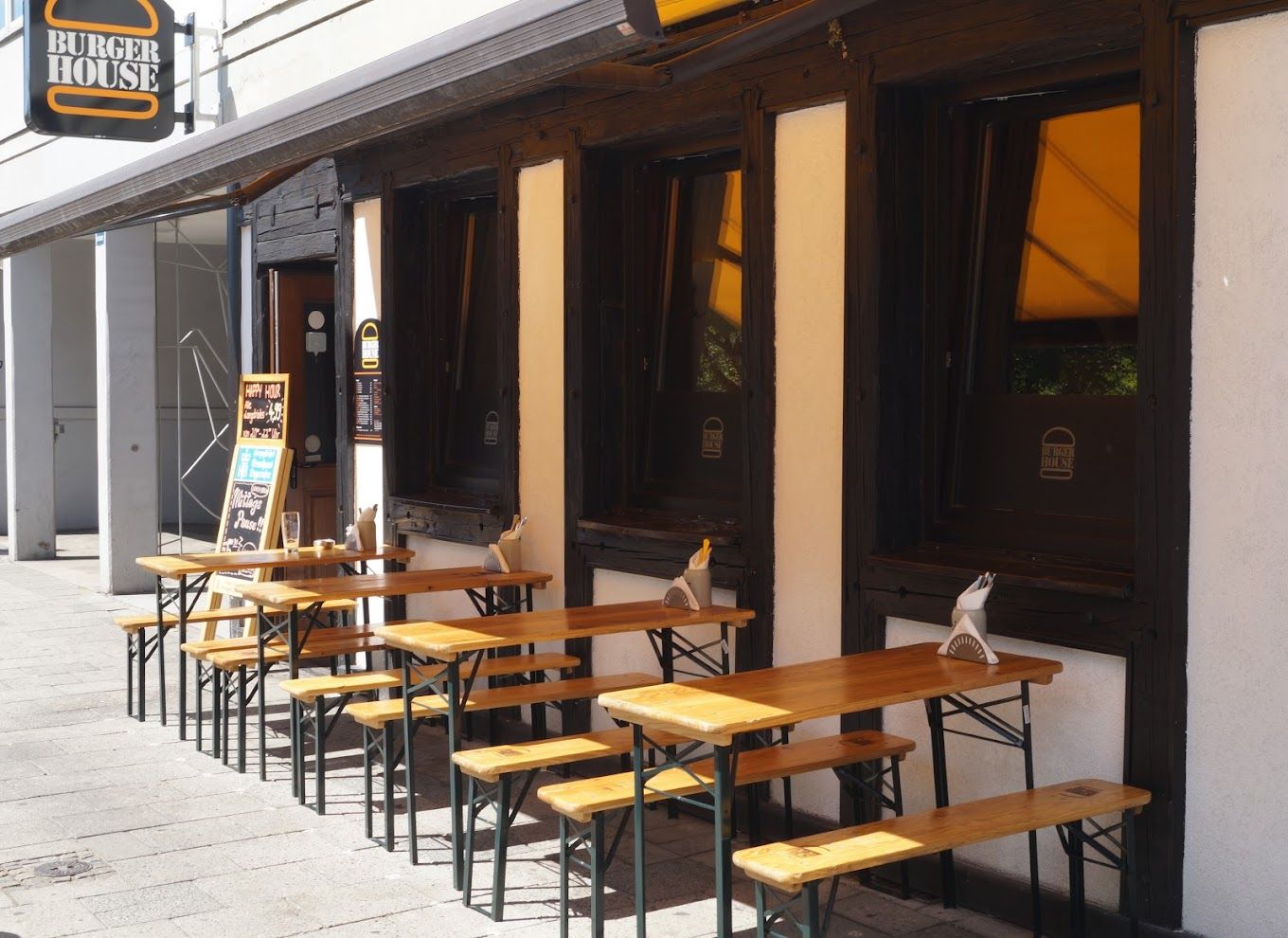 Außengastronomie des "Burger House" mit Holzbänken und -tischen vor der Fassade.
