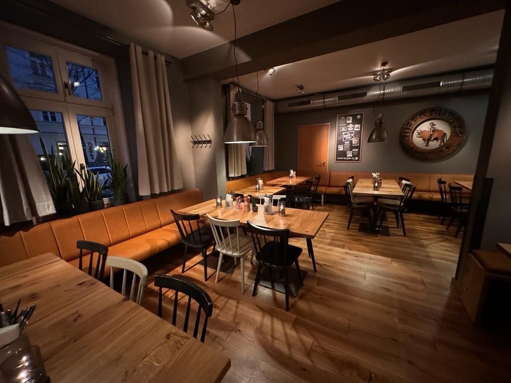 Innenansicht von "Ruff's Burger" mit Holztischen, schwarzen und weißen Stühlen, Polsterbänken, Wandlogo und Hängelampen.