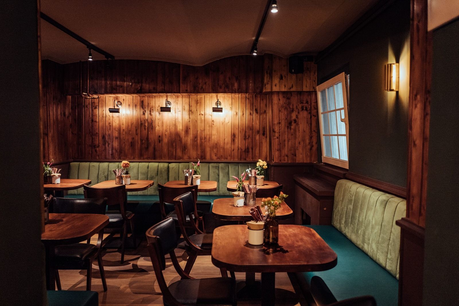 Innenansicht von "Otto's Burger" mit mehreren grünen Polsterbänken, Holztischen, Stühlen und vertäfelter Holzverkleidung.