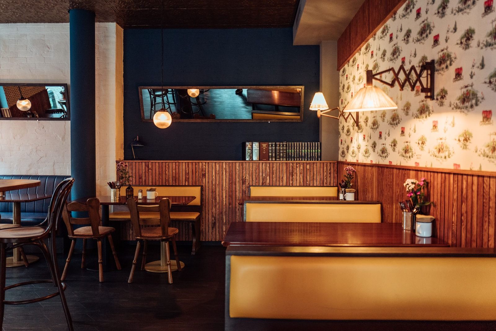 Innenansicht von "Otto's Burger" mit gelben Polsterbänken, gemusterter Tapetenwand, Holzvertäfelung und Holztischen.