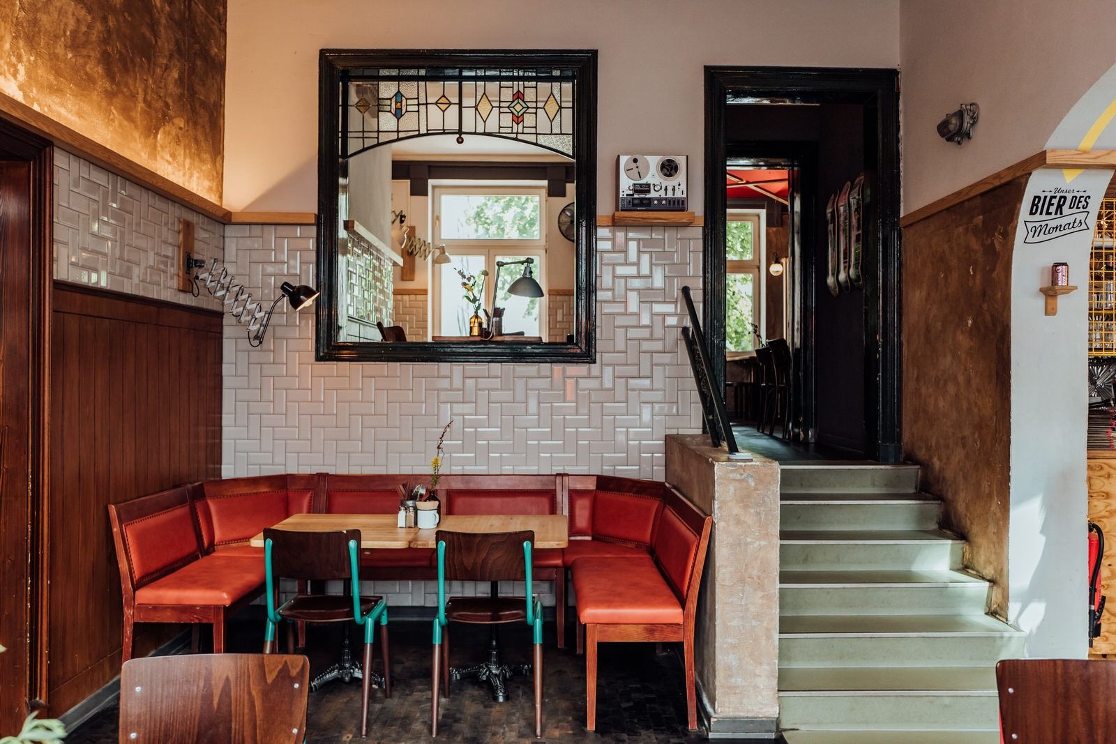 Innenansicht von "Otto's Burger" mit roter Sitzecke, weißen Wandfliesen, Durchgangsfenster, Treppe und Dekoelementen.